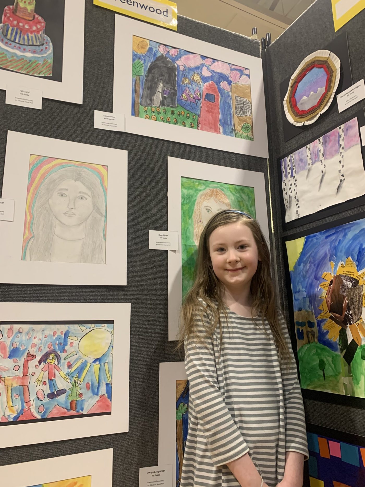 A student poses next to her artwork displayed at the DMPS Art Show.